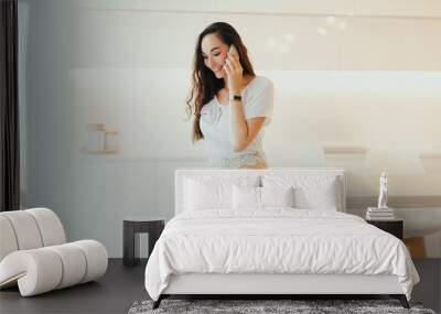 Happy young beautiful woman speaks on phone in minimalistic light kitchen Wall mural