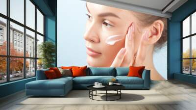 Young beautiful woman applies cream on clean perfect skin Wall mural