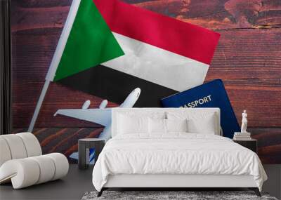 Flag of Sudan with passport and toy airplane on wooden background. Flight travel concept Wall mural