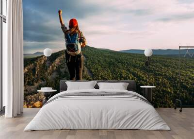 A traveler with a backpack in the mountains at sunset. A traveler with a backpack on the background of mountains, rear view. Hiking trips. A tourist girl on the background of a mountain landscape Wall mural