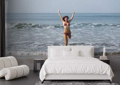 Slender young girl in a swimsuit is jumping on the sandy shore of the ocean. Happy Days. The concept of freedom, recreation, vacation. Flight of joy and fun. Reflection in water. Charming smile. Wall mural