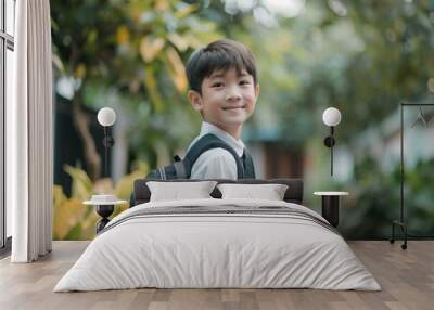 Asian teen boy wearing school uniform with backpack stands in nature landscape. Looks back at camera with serious expression. Trees, bushes surround with building peeking out from behind foliage. Wall mural