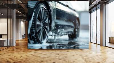 Black car side cleaning with foam soap close-up. Wet surface and soap suds on tires and car body. Parking lot or garage background blurred. Side view of vehicle shows tire and soap bubbles. Wall mural