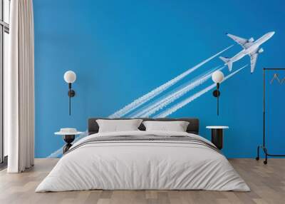 White aircraft flies at distance in clear blue sky with contrails. Panoramic view of airplane in flight. Condensation trails stream behind jet in blue sky. Wall mural