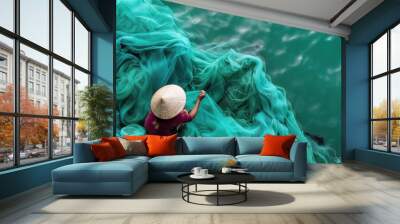 Woman sits on rock, holding fishing net near turquoise water. She gazes at green water, net spread out in front. Scene captures peaceful atmosphere of fishing dock in Vietnam. Wall mural