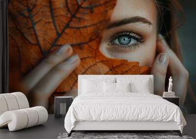 a woman is hiding half of her face behind an orange autumn leaf. Fall season concept Wall mural