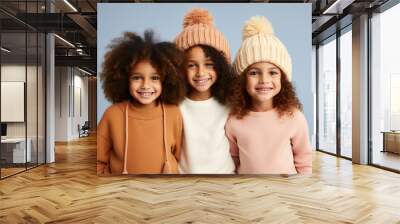 Three little girls wearing comfy warm clothes and wool hats in pastel colors, posing and smiling. Fall winter fashion for kids. Generative AI Wall mural