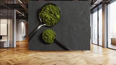 Chlorella green powder in spoons on a black stone background. Spirulina powder algae or barley. Superfood. Copy space, top view, flat lay. Wall mural