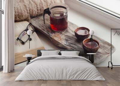 Still life details, cups of asian tea and teapot on vintage wooden tray on windowsill in living room. Lazy winter weekend with a book at home Wall mural