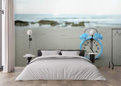 Blue vintage alarm clock on the beach in evening time with sunlight. Summer travel concept. Vacation and holiday concept. Get off work concept. Wall mural