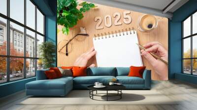 New year resolutions 2025 on desk. 2025 goals - hands and notebook, coffee cup, plant on wooden table. Resolutions, plan, goals, action,  idea concept. New Year 2025 resolutions, copy space Wall mural