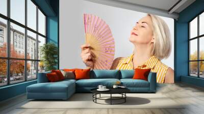 Attractive middle aged woman relaxing with fan. Mature woman experiencing hot flush from menopause isolated Wall mural