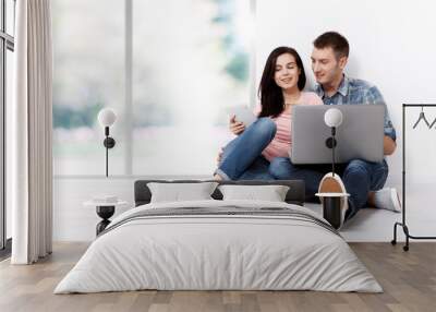 Happy young couple sitting on the floor with a laptop looking for their new home and furniture. Mock up for design. Wall mural