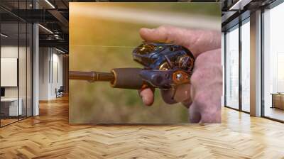 hand with spinning and reel on the evening summer lake. Fishing on the lake at sunset. Fishing background. Wall mural