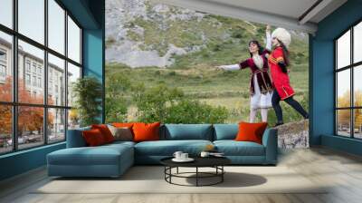 Young girls in national costumes dance a beautiful dance at the foot of the mountain on the ruins of a residential barrack Wall mural