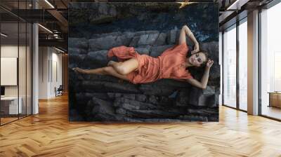 Beautiful young brunette woman with orange dress on a rock nature background Wall mural