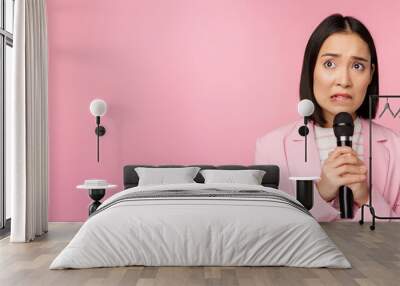 Anxious asian lady in suit, talking in public, giving speech with microphone on conference, looking scared, standing over pink background Wall mural