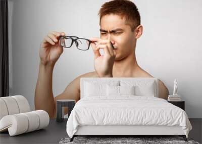 Beauty, people and lifestyle concept. Portrait of young handsome asian man with naked torso, waking up morning cant see anything without glasses, squinting put on eyewear, white background Wall mural