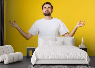 Caucasian young man white t-shirt standing isolated on gray studio background, folding fingers breath exercises process for reducing stress Wall mural