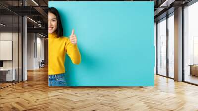 Cheerful asian female model showing thumbs up gesture, smiling and looking impressed, praise good product, standing over blue background Wall mural