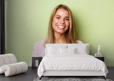 Close-up of stylish blond girl smiling, looking confident, standing over green background Wall mural