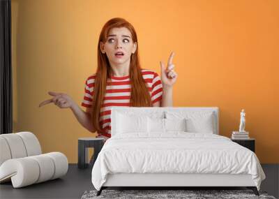 Complicated questioned redhead girlfriend trying understand what happening, which way go, look around, pointing sideways up and right, frowning perplexed, taking hard decision, orange background Wall mural