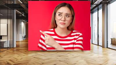 Disappointed doubtful frowning asian girl asking question reassure, looking pointing left displeased, unimpressed with strange place, dislike interiour sulking distressed, stand red background Wall mural