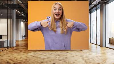 Excited fascinated european cute young girl blond hair smiling open mouth amused telling look down pointing downwards amazing cool new product recommend advertisement, orange background Wall mural