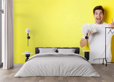 Excited man holding money, showing thumb-up in approval, got credit or loan, standing over yellow background Wall mural