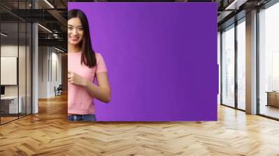 Friendly cute pleasant asian woman showing way, indicating interesting promo, pointing left smiling broadly, introduce advertisement product, stand purple background cheerful Wall mural