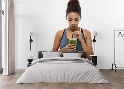 Healthy and Fitness concept - Beautiful American African lady in fitness clothing drinking healthy vegetable drink. Isolated on white background. Wall mural