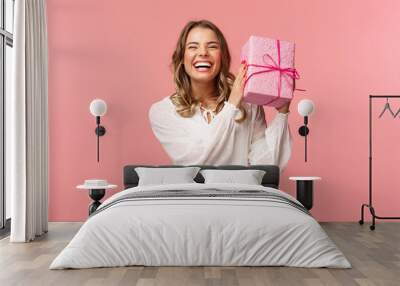 Holidays, celebration and women concept. Portrait of happy charismatic blond girl shaking gift box wondering whats inside as celebrating birthday, receive b-day presents, pink background Wall mural