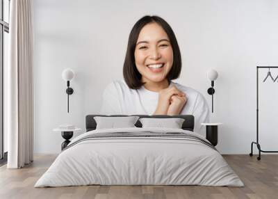 Portrait of beautiful korean woman with healthy white smile, laughing and looking happy at camera, standing in tshirt over white studio background Wall mural