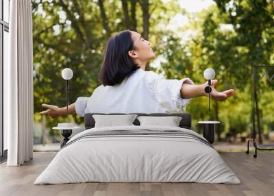 Portrait of carefree young asian woman dancing in park alone, enjoying freedom, smiling with joy Wall mural