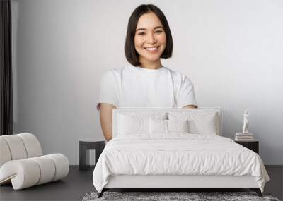 Portrait of happy asian woman smiling, posing confident, cross arms on chest, standing against studio background Wall mural