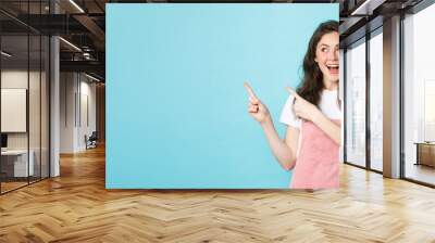 Portrait of happy smiling female model with glamour blush, pointing fingers left and looking at promo offer, showing an advertisement copy space, blue background Wall mural