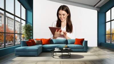 Portrait of smiling corporate woman looking at digital tablet, working, standing over white background Wall mural