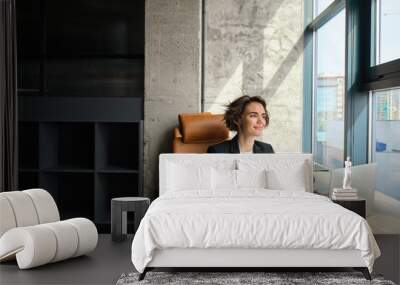 Portrait of successful lady boss, businesswoman in an office, working on her laptop, looking outside window, signing documents and papers Wall mural