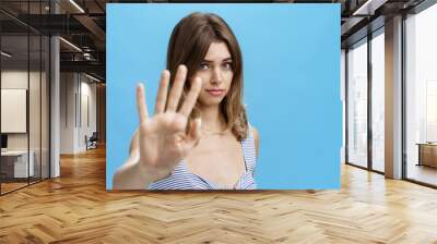 Silly and shy insecure attractive girl pulling hand towards to cover face from camera making moody timid expression asking to stop not liking what happening saying no with body language over blue wall Wall mural