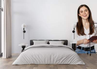 Smiling modern woman standing with digital tablet, laughing and looking happy, working, posing against white studio background Wall mural