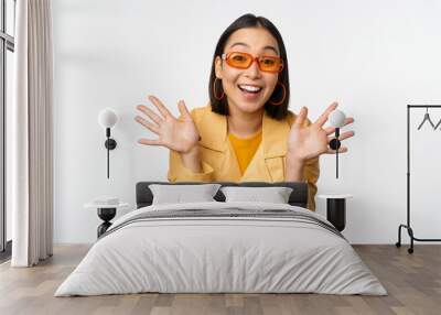 Surprised jazz hands. Happy asian girl smiling, looking amazed at camera, announcing smth, standing over white background Wall mural