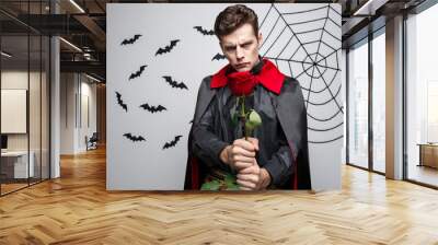 Vampire Halloween Concept - Portrait of handsome caucasian Vampire holding red beautiful rose. Wall mural