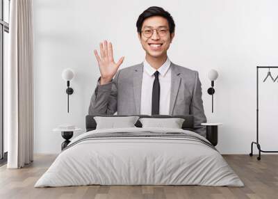 Waist-up portrait of friendly, cheerful smiling asian male entrepreneur, office worker saying hi, greeting coworker waving hand in hello, welcome gesture, standing white background Wall mural