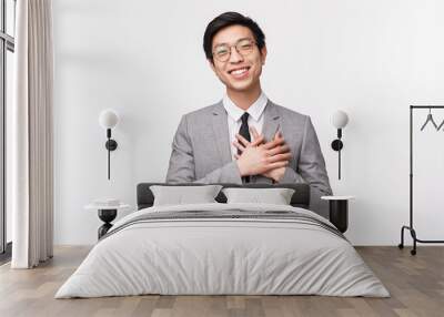 Waist-up portrait of grateful, flattered asian young male office manager, entrepreneur hold hands on heart and smiling, thanking for compliment, flattered and grateful for praises, white background Wall mural