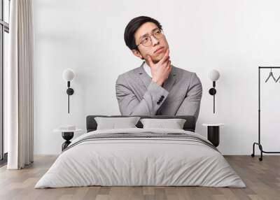 Waist-up portrait of thoughtful, creative and smart asian young man in grey suit, office manager, businessman planning project, thinking looking up pondering ideas, white background Wall mural