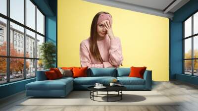 Woman facepalming covering face annoyed, bothered and inrritated, smirking looking with dismay, pissed off, posing unhappy displeased, staring indignant and upset posing tired over yellow background Wall mural