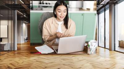 Young corporate woman working from home. Asian girl has online classes remotely, talking on video chat, internet lecture or webinar Wall mural