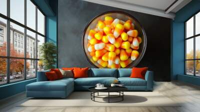 A bowl of candy corn is sitting on a black table. The bowl is filled with many different colored corn kernels, including yellow and orange Wall mural