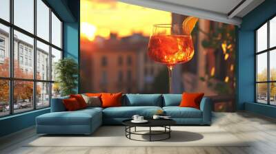 A glass of wine with an orange slice in it is sitting on a railing. The sun is setting in the background, creating a warm and inviting atmosphere Wall mural