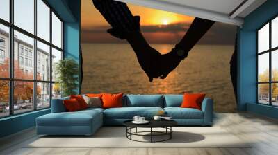 A loving couple (silhouettes of a man and a girl) hold hands in the rays of light at sunset on the sea on a pier. Wall mural